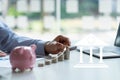 Businessman holding coins on pile of money-saving ideas and planning to buy a pink piggy bank house save money to spend and Money