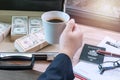 businessman holding cup of hot coffee with banknote on the bag and glasses , passport, pen and document on wooden table Royalty Free Stock Photo