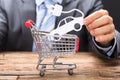 Businessman Holding Electric Paper Car Over Shopping Cart