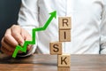 Businessman holding a green up arrow near the word Risk. Improving business resilience, reducing risks and costs. Development