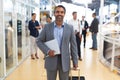 Businessman holding laptop and trolley bag and looking at camera in a modern office Royalty Free Stock Photo