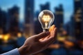 Businessman holding a light bulb in his hand on blurred city background, Hand holding a glowing light bulb against an abstract Royalty Free Stock Photo