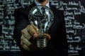 Businessman Holding Light Bulb in Front of Blackboard. Generative AI Royalty Free Stock Photo