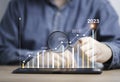 Businessman holding magnifier glass to find virtual increasing technical graph and up arrow for trader analysis to searching the Royalty Free Stock Photo