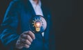 Businessman holding a magnifying glass that illuminates a light bulb icon, representing insight, innovation, and the search for Royalty Free Stock Photo
