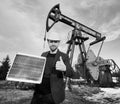 Businessman standing on an oilfield holding mini solar module next to an oil rig Royalty Free Stock Photo