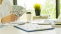 A businessman holding money offering banknotes to someone Hand paying dollar bills on a desk with graphs and a laptop, a tiger ski Royalty Free Stock Photo