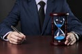 businessman holding pen at his arm and hourglasses standing on a table. deadline concept