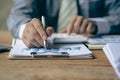 Businessman holding pen and paper pointing chart summary analysis calculating annual business report using laptop at desk in offic Royalty Free Stock Photo