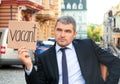 Businessman holding piece of cardboard with word VACANT while sitting in office armchair outdoors