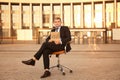 Businessman holding piece of cardboard with word VACANT while sitting in office armchair outdoors