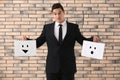 Businessman holding sheets of paper with drawn emoticons against brick wall Royalty Free Stock Photo