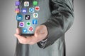 Businessman holding smart phone from which flying social media apps icons, on grey background, social media in smart phone concept