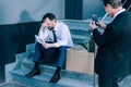 Businessman holding smartphone holding smartphone and photographing upset fired colleague sitting on stairs