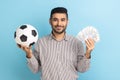 Businessman holding soccer ball and fan of dollar bills, sports betting, big win, looking at camera. Royalty Free Stock Photo