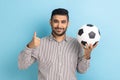 Businessman holding soccer ball on his hand with smiling positive expression, showing thumb up. Royalty Free Stock Photo