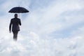 Businessman holding an umbrella and walking away in dreamlike clouds Royalty Free Stock Photo
