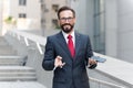 Businessman holding up credit card and making online payment on his cellphone with building background. Royalty Free Stock Photo