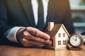 Businessman holding a wooden house and clock. Mortgage, real estate and loan concept. Tax payment. Construction investment. Royalty Free Stock Photo