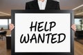 Businessman holds a big signboard with help wanted message. Business recruitment or employment