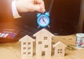 Businessman holds clock over wooden houses. Time to pay taxes. Mortgage. Payment of debts for real estate. Payment of utility