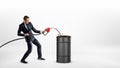 A businessman holds a gas nozzle and overfills a black barrel with oil. Royalty Free Stock Photo