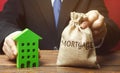 Businessman holds a money bag with the word Mortgage and a wooden house. Real estate concept. Loan for apartment and housing.