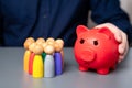 A businessman holds a red piggy bank next to a group of people figures.