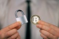 A businessman holds a silver padlock and physical version of bitcoin in his hands. Prohibition of cryptocurrencies, regulations,