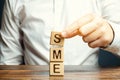 Businessman holds wooden blocks with the word SME. Small and medium-sized enterprises - commercial enterprises that do not exceed