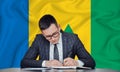 A businessman in a jacket and glasses sits at a table signs a contract against the background of a flag Saint Vincent and the