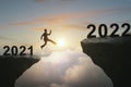 Businessman jumping from 2021 cliff to 2022 New Year on sky background. Gap, leap, risk, challenge and success concept Royalty Free Stock Photo