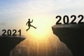 Businessman jumping from 2021 cliff to 2022 New Year on beautiful sky and city background. Gap, leap, risk, challenge and success Royalty Free Stock Photo
