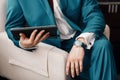 Businessman keep a digital tablet in hand whilst sitting on a sofa in a blue suit. on hand expensive mechanical watch