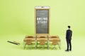 Businessman looking at abstract chalkboard display smartphone, wooden desk and chairs on green background. Online education, Royalty Free Stock Photo