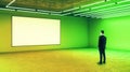 Businessman looking at white mock up poster on light green wall in empty hall with neon paints Royalty Free Stock Photo