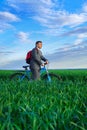 A businessman looks into the distance, he is standing with a backpack and a bicycle on a green grass field, dressed in a business Royalty Free Stock Photo