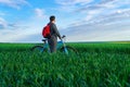 A businessman looks into the distance, he is standing with a backpack and a bicycle on a green grass field, dressed in a business Royalty Free Stock Photo