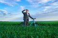 A businessman looks into the distance, he is standing with a backpack and a bicycle on a green grass field, dressed in a business Royalty Free Stock Photo