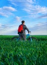 A businessman looks into the distance, he is standing with a backpack and a bicycle on a green grass field, dressed in a business Royalty Free Stock Photo