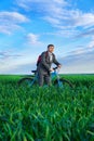 A businessman looks into the distance, he is standing with a backpack and a bicycle on a green grass field, dressed in a business Royalty Free Stock Photo
