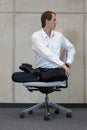 Businessman in lotus pose on office chair practicing yoga