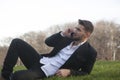 Businessman is lying on a meadow in a city-park and talks on a smart phone