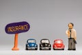 Businessman made from plasticine next to three cars and an insurance sign , on white background