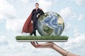 Businessman in mask and cape standing and resting one elbow on Earth globe, on top of digital tablet screen covered with Royalty Free Stock Photo