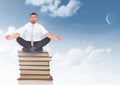 Businessman meditating sitting on Books stacked by blue sky Royalty Free Stock Photo