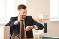 Businessman with mobile phone looking at his wristwatch in office. Time management concept Royalty Free Stock Photo