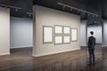 Businessman in modern concrete exhibition hall interior looking at blank white mock up posters on wall and wooden flooring with Royalty Free Stock Photo