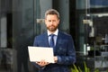 Businessman with notebook outdoor. Confident business expert. Handsome man in suit holding laptop against office Royalty Free Stock Photo
