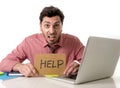 Businessman at office desk working on computer laptop asking for help holding cardboard sign looking sad and depressed Royalty Free Stock Photo